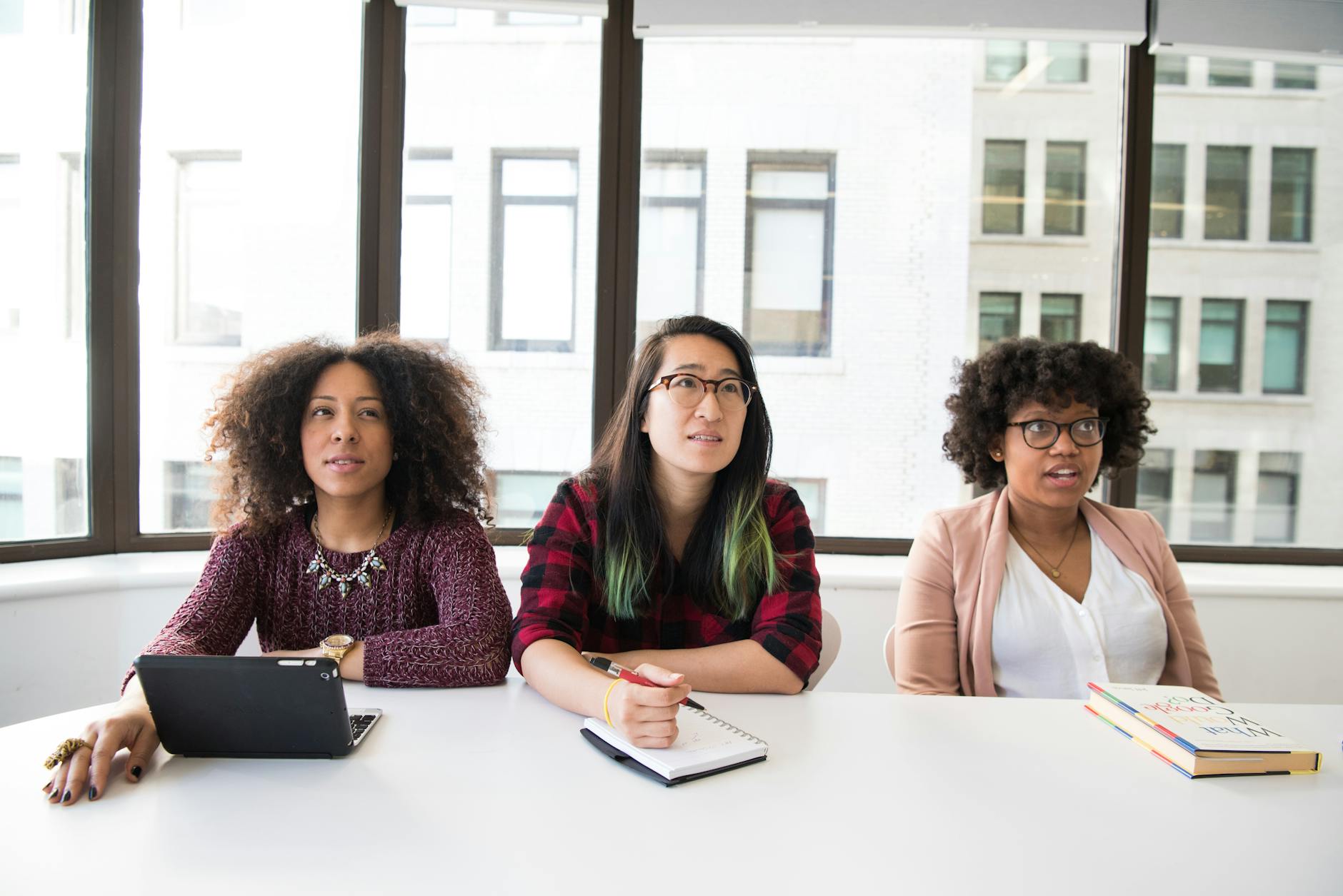 Three women engaged in a thoughtful meeting in a modern office setting.